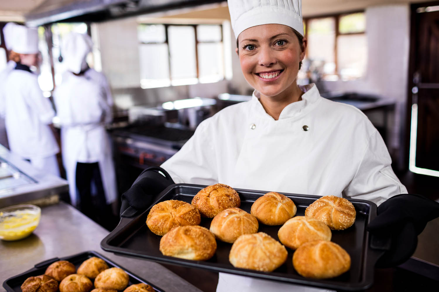 Female chefs holding baking tray of kaiser rolls in kitchen at hotel